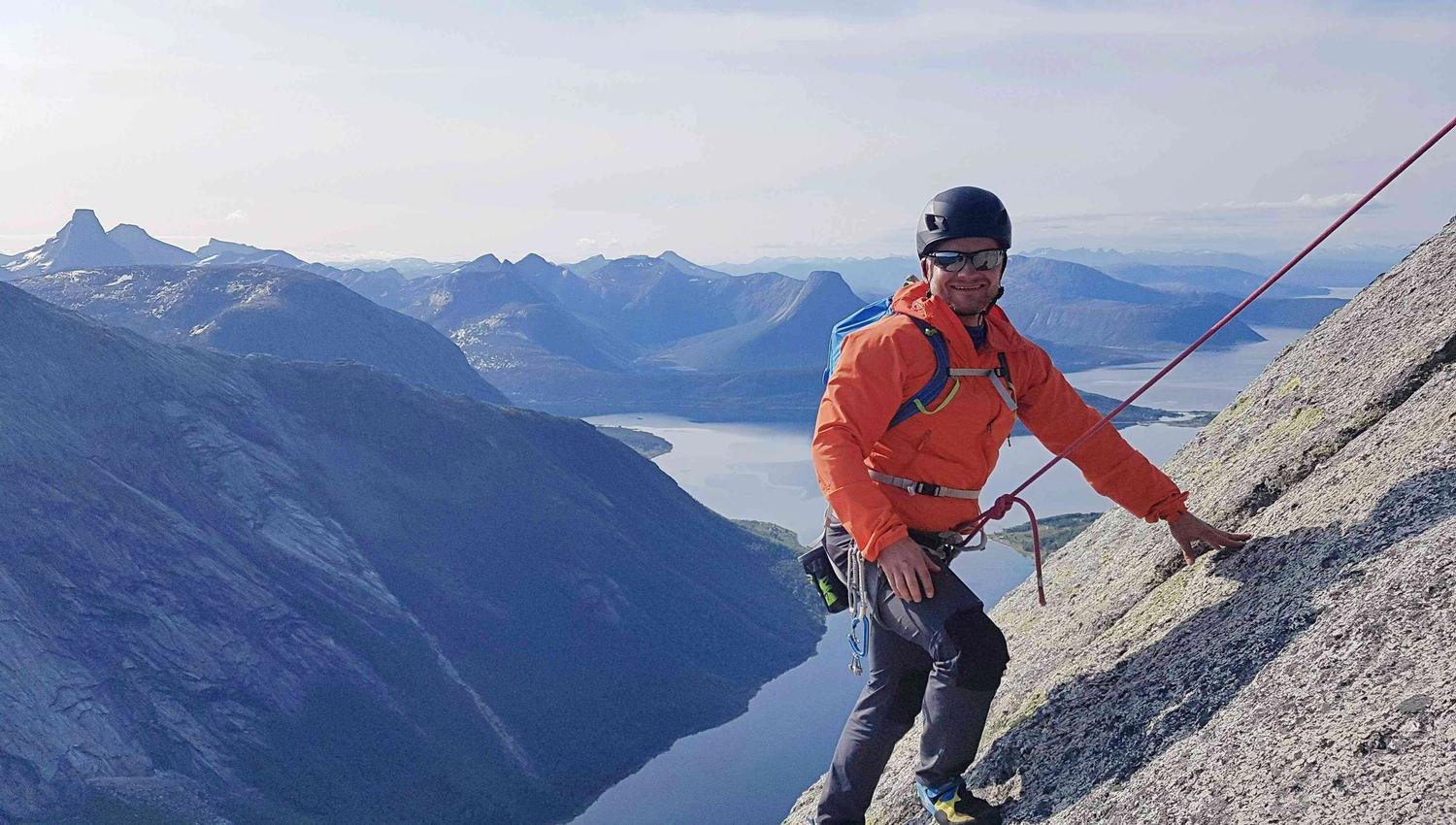 En mann klatrer opp en fjellside iført klatreutstyr.