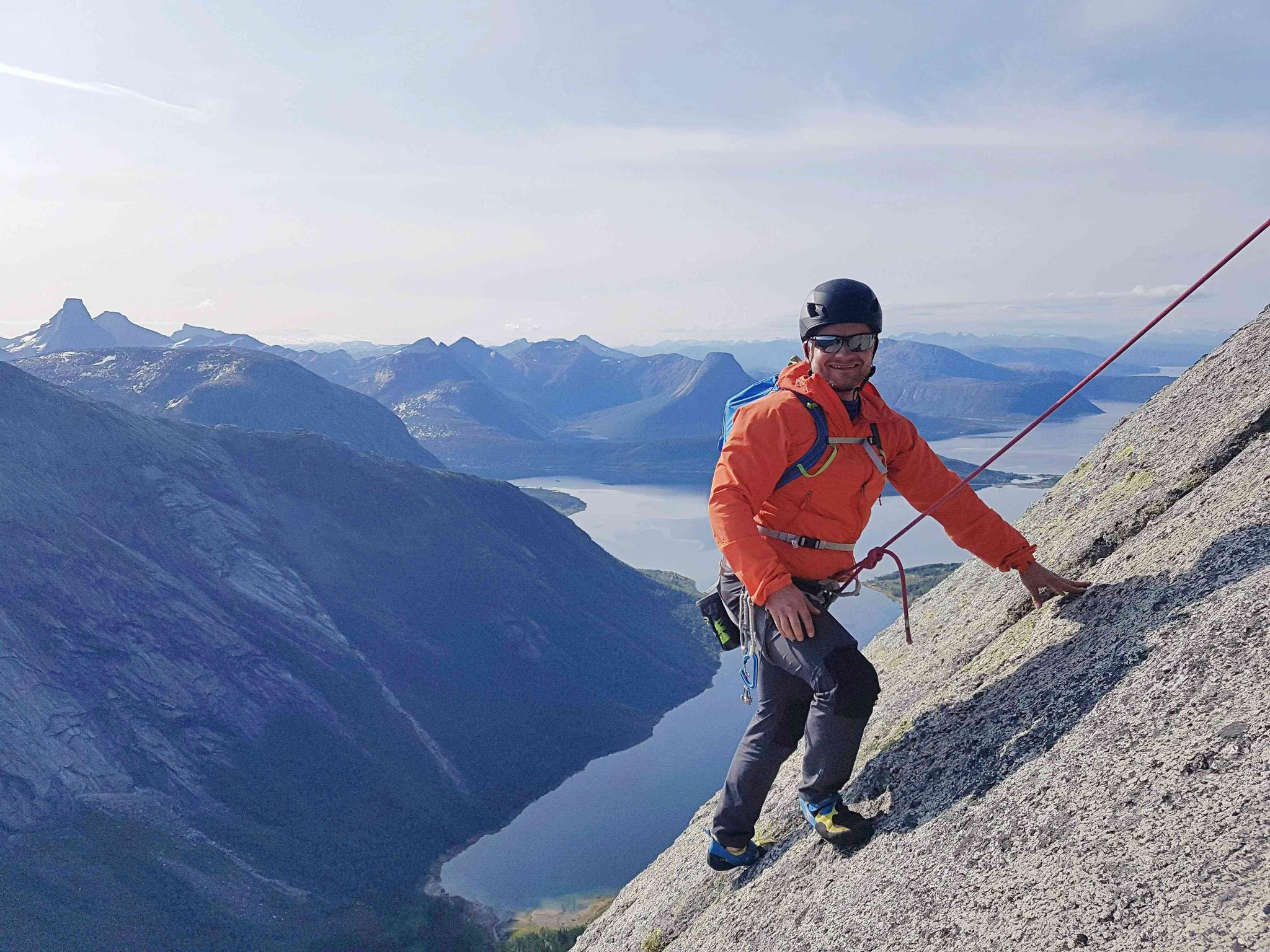 A man climbing up a mountainside with climbing gear on.