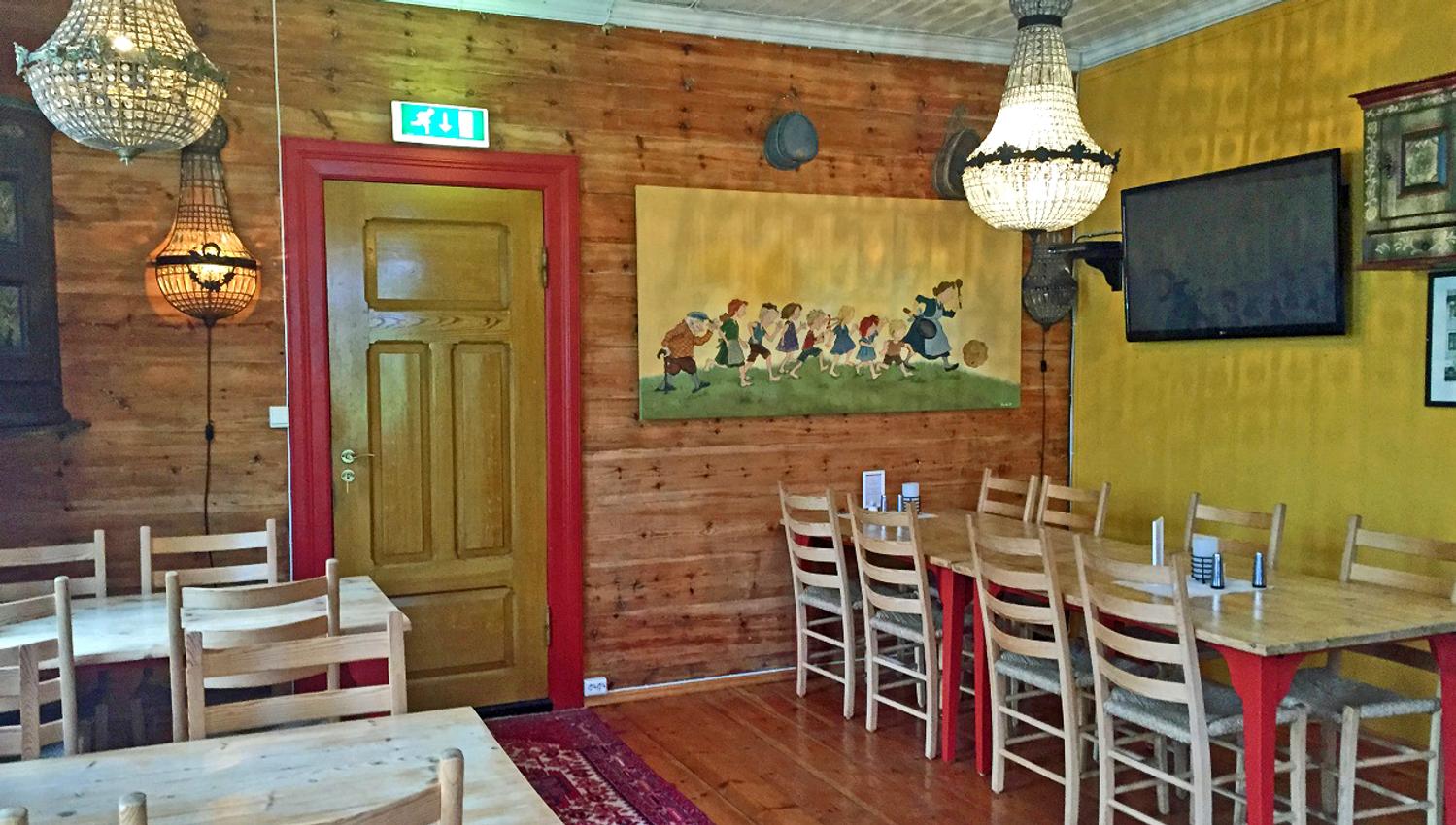 Inside the pancake restaurant. Tables and chairs. A funny painting with a woman and children running after a rolling pancake.