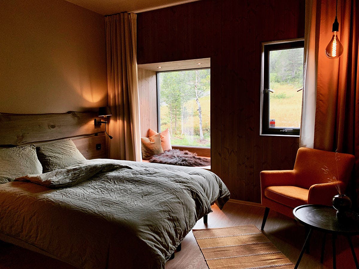 Chambre moderne avec lit, fenêtre donnant sur la nature, et fauteuil orange.