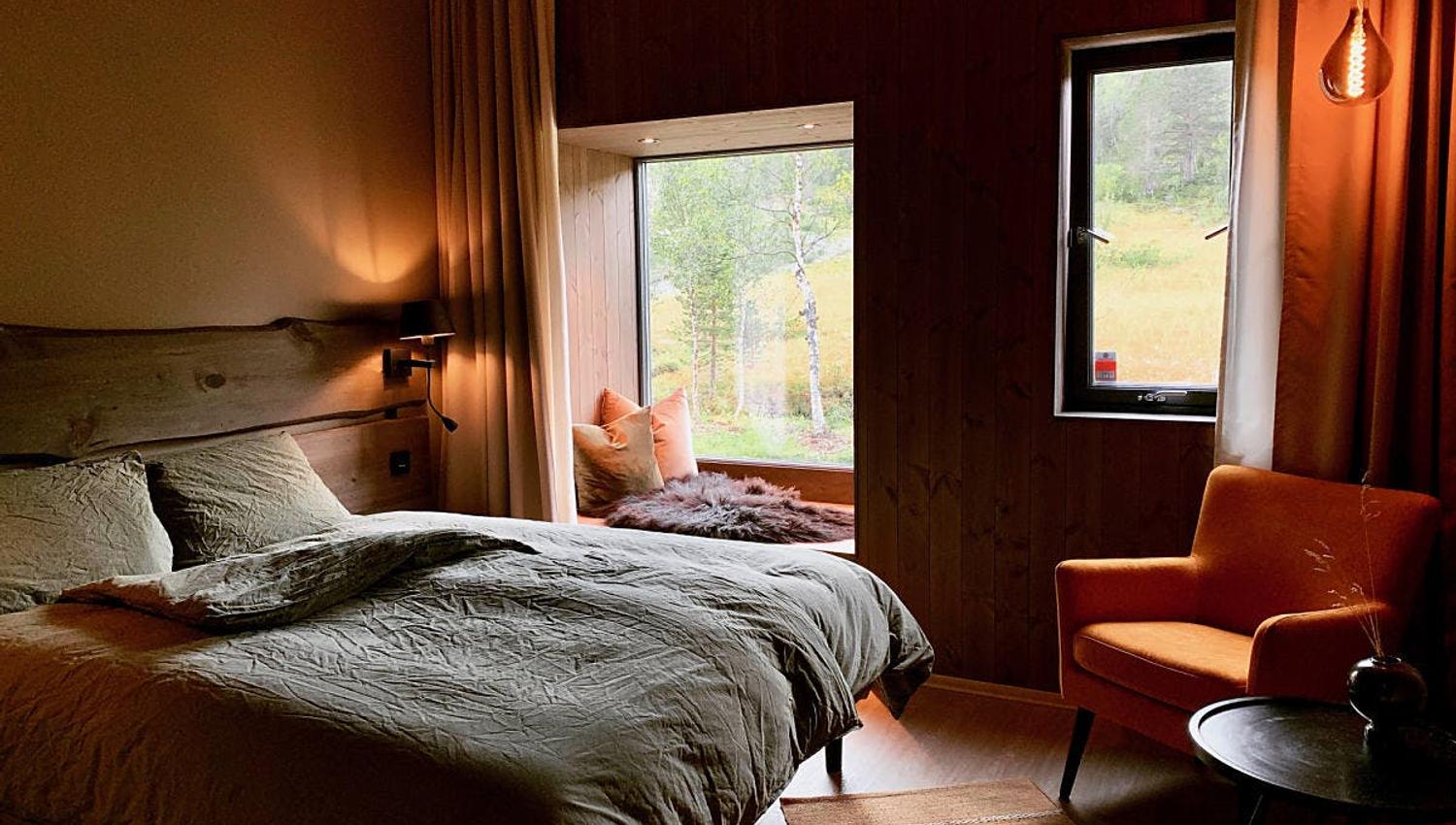 Chambre moderne avec lit, fenêtre donnant sur la nature, et fauteuil orange.