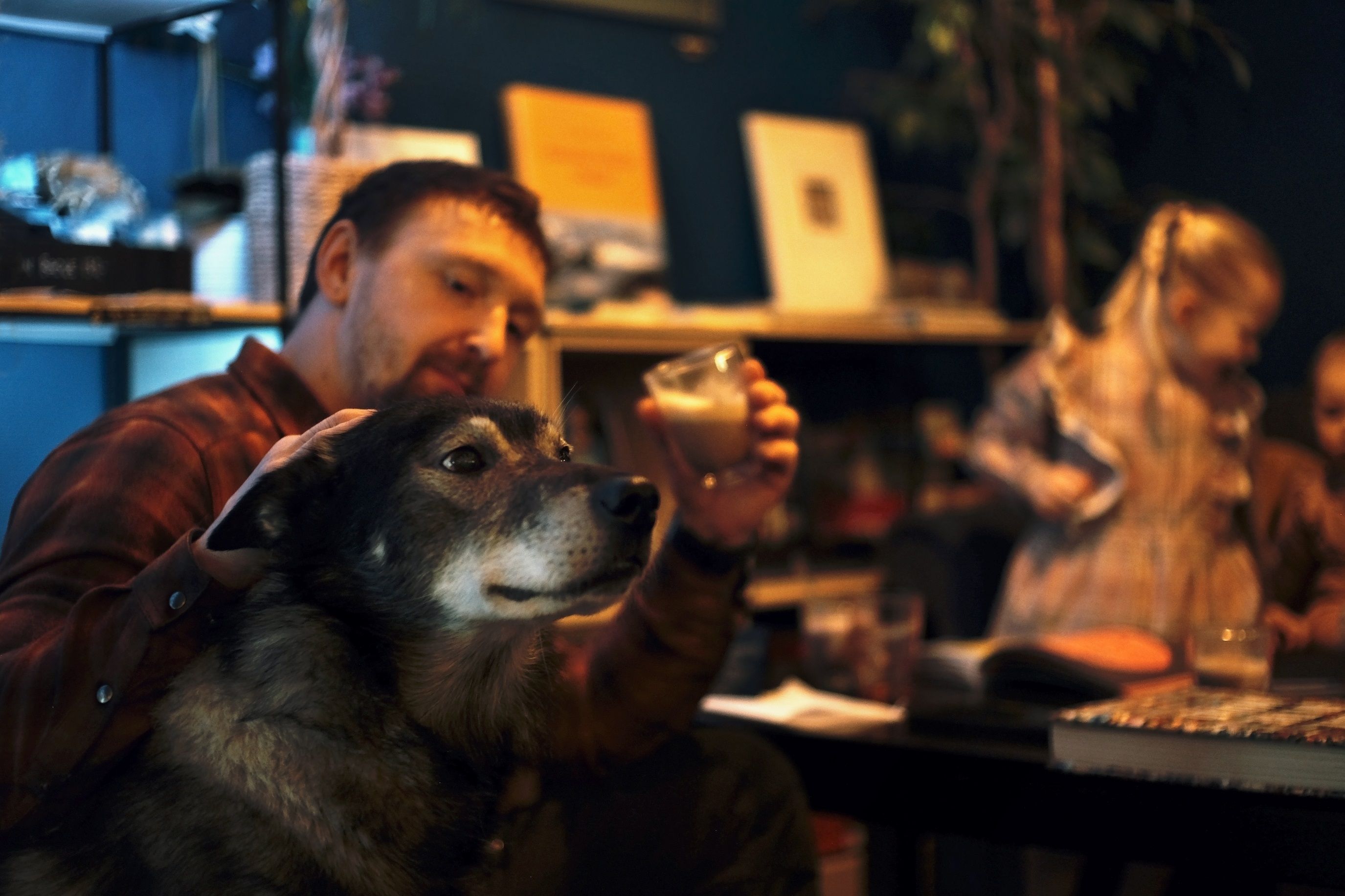 A person holding a cup of coffee while petting a husky in the foreground.