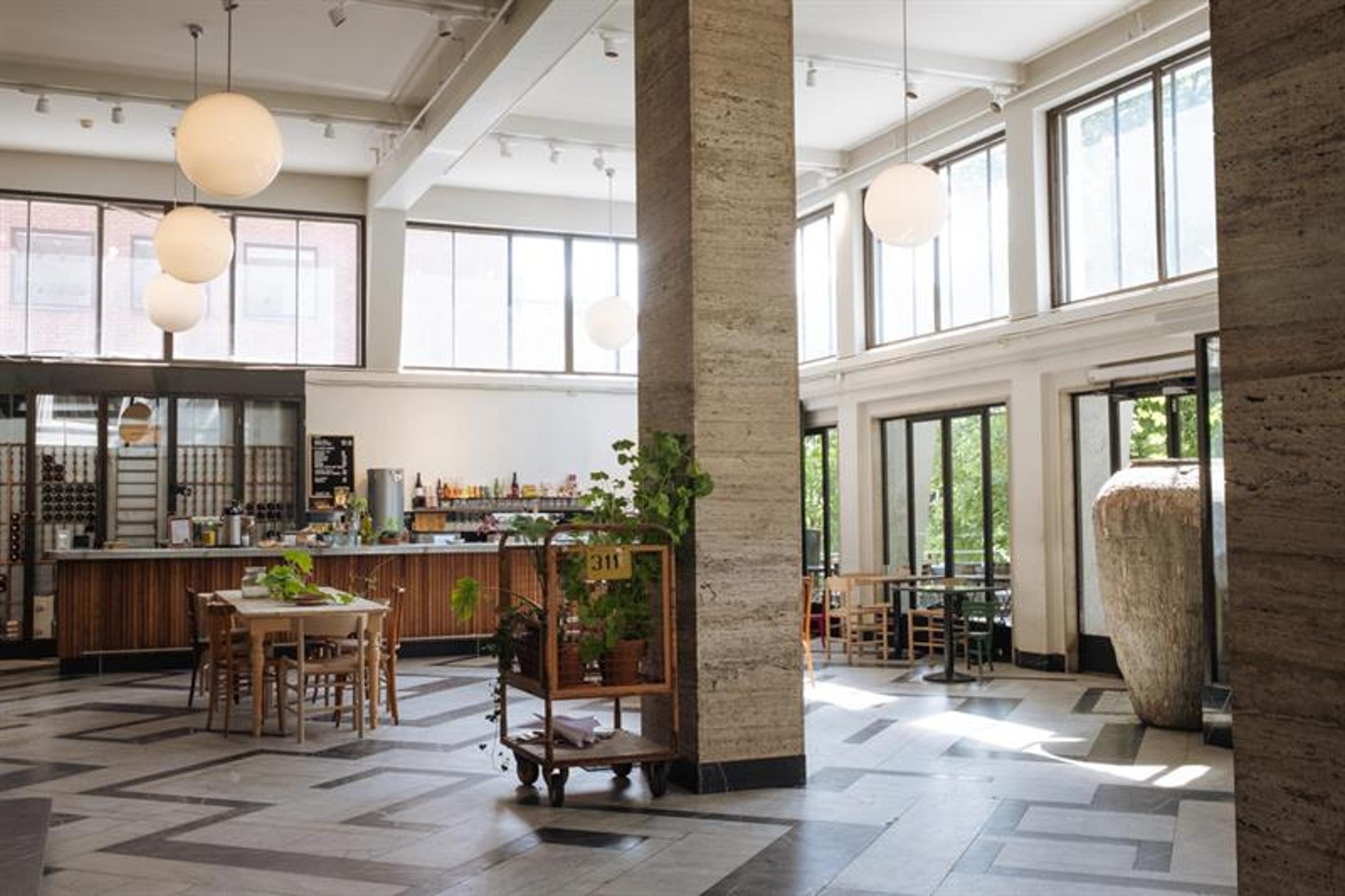 Café interior with a high ceiling, square pillars, globe-shaped ceiling lamps, a bar counter, square tables, and large windows