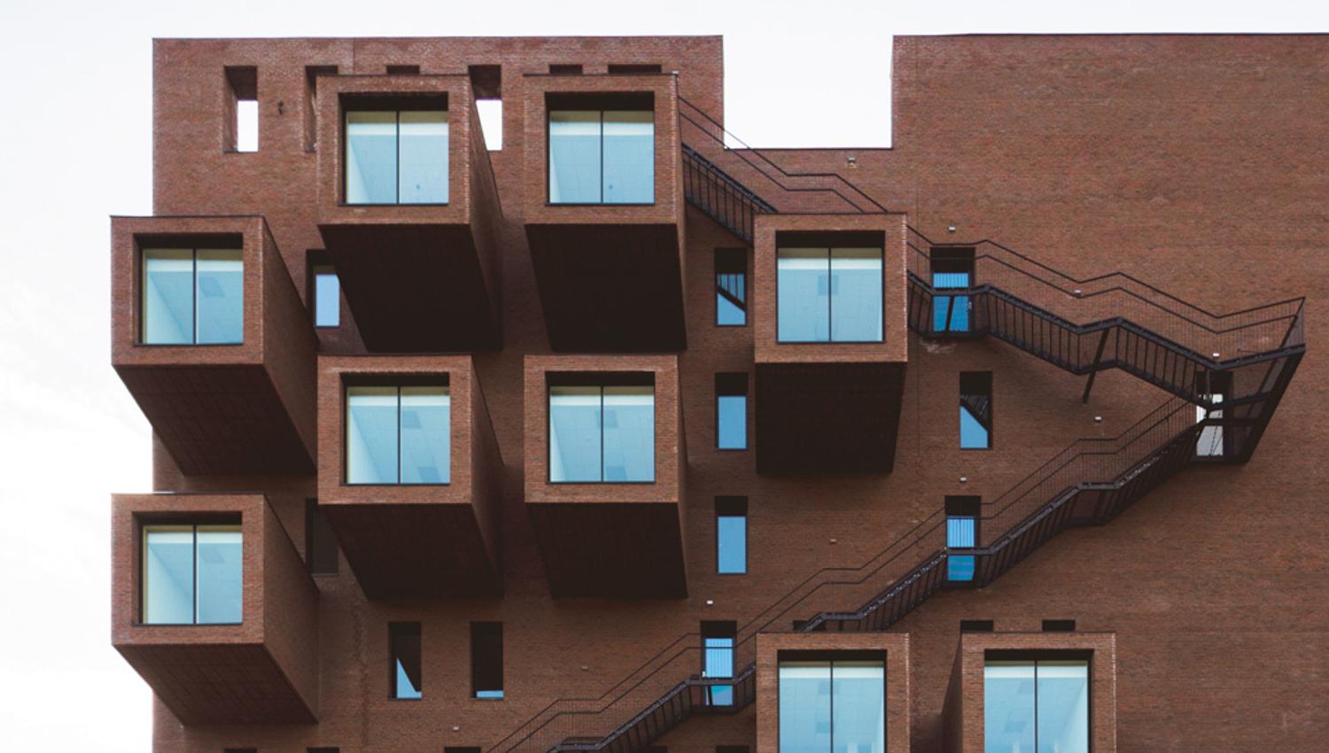Brown building with outside stairs and large windows.