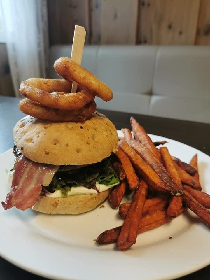 Sandwich burger topped with onion rings on a pick, served on a white plate with fries on the side.