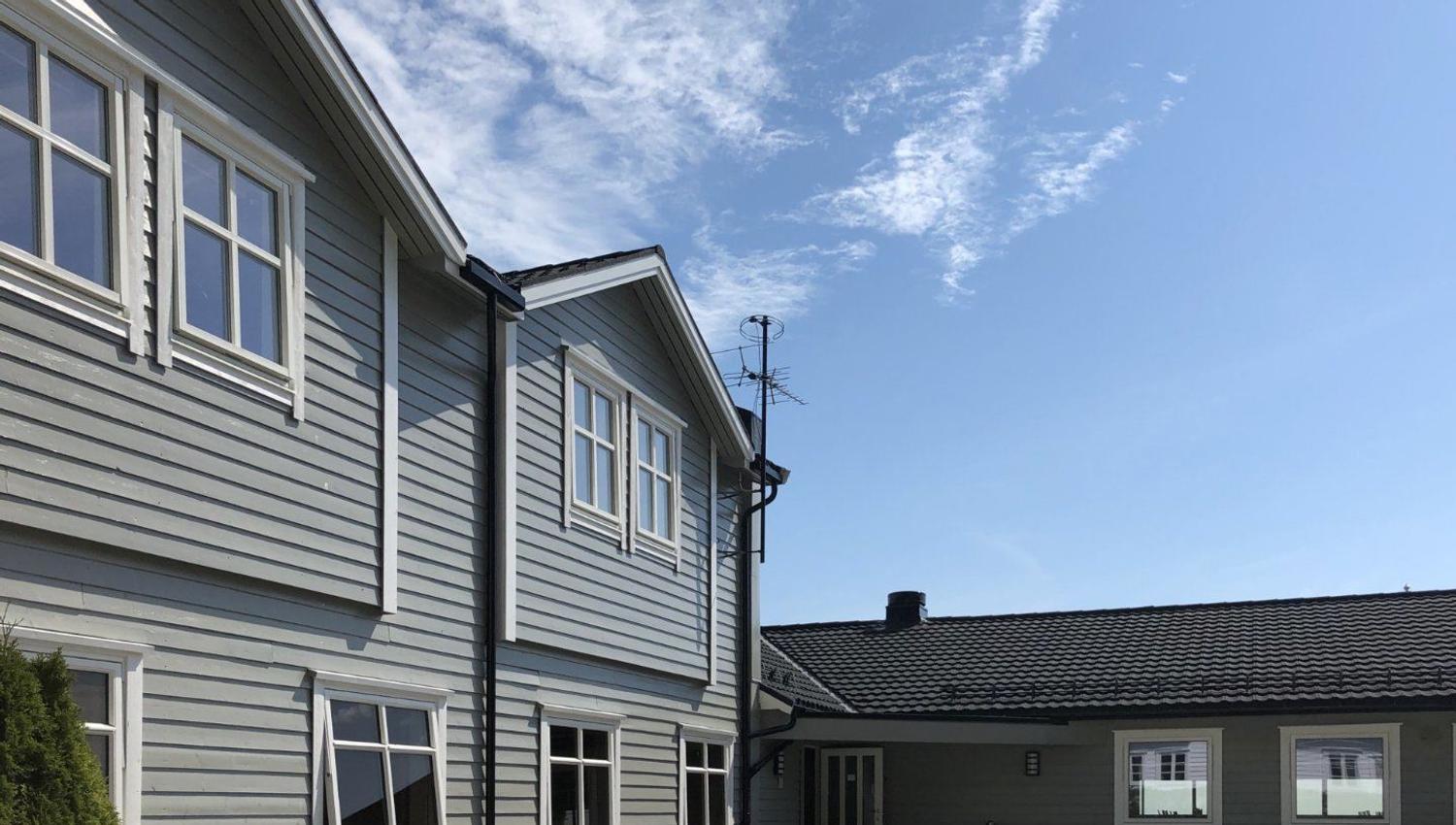 Exterior of a gray wooden house with white-trim windows, a courtyard, and blue sky with wispy clouds..