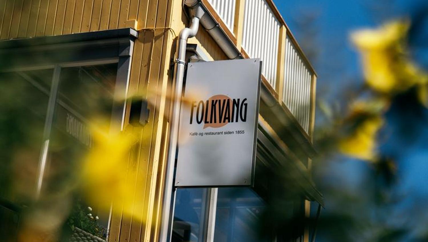 Skiltet til Folkvang – kafé og restaurant siden 1855 – montert på byggets fasade omgitt av blomster.
