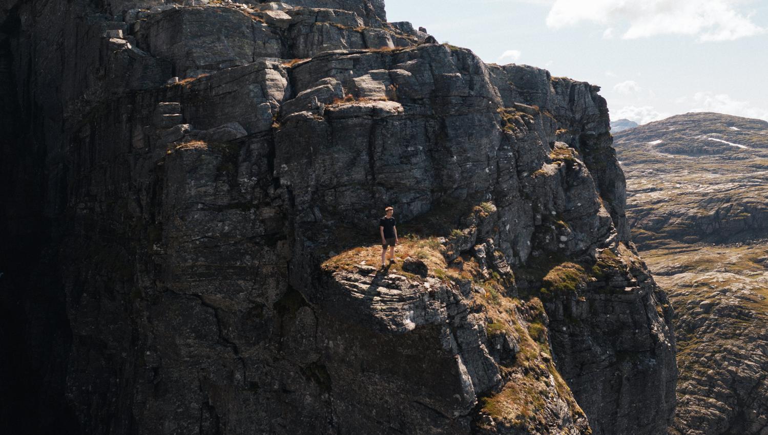 Person står på fjellformasjon og ser utover fjellandskapet.