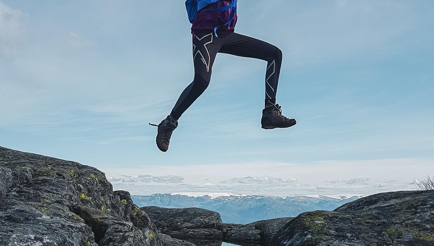 Person jumping across a mountain pond in Hardanger, Norway, capturing joy and outdoor adventure
