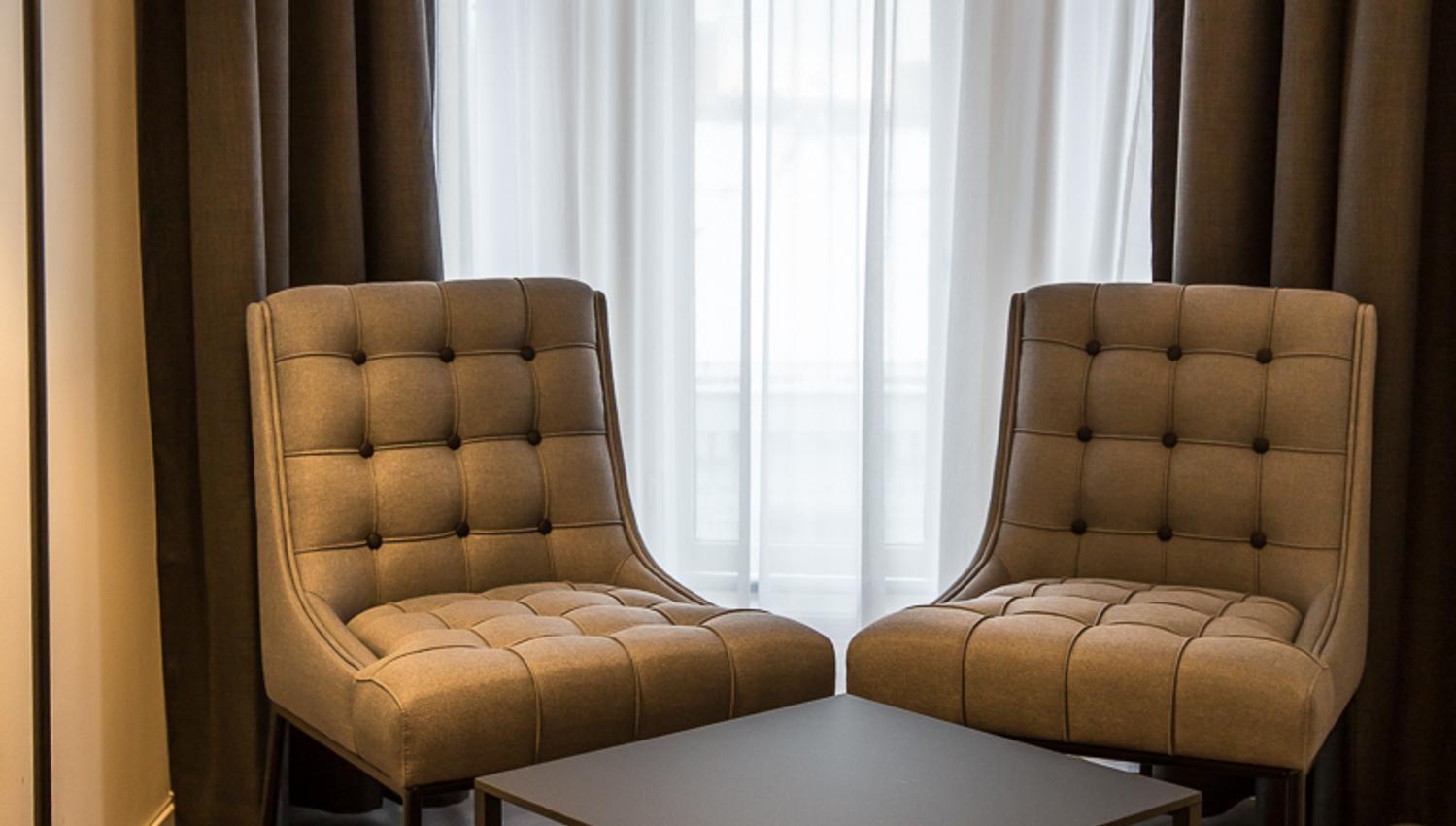 Two brown chairs, coffee table and lamp in front of a window. Saga Hotel & Poshtel Oslo Central. Photo