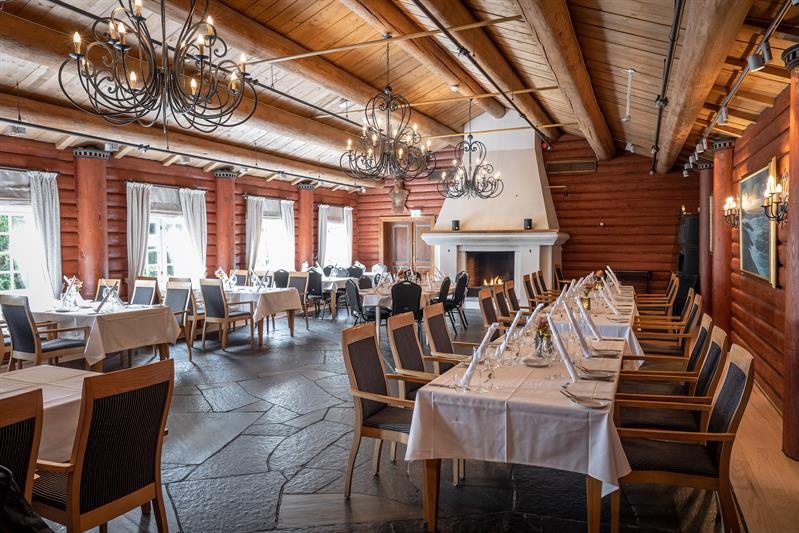 Restaurant med peis og dekket bord med stoler. Laftede tømmervegger