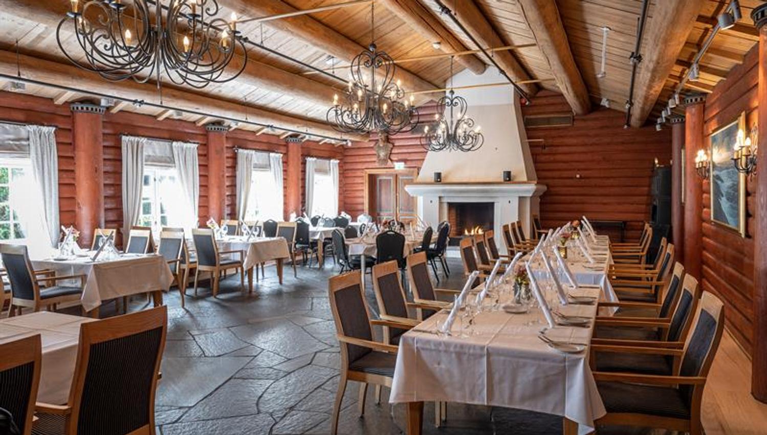 Restaurant med peis og dekket bord med stoler. Laftede tømmervegger