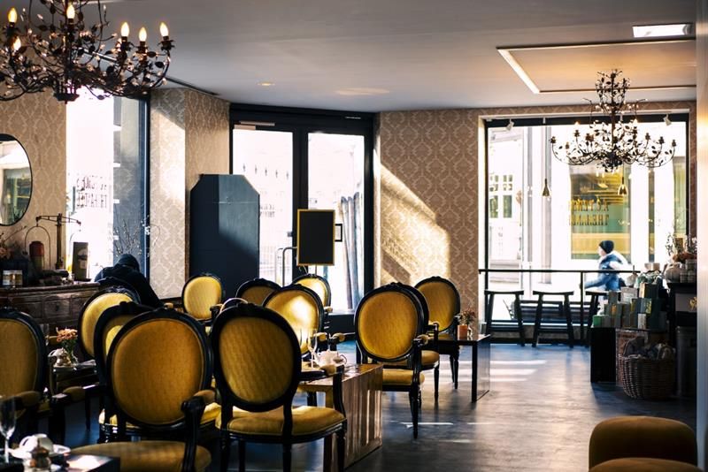 Interior: Yellow upholstered antique chairs and tables, chandeliers hanging from the ceiling.