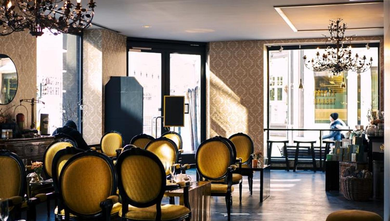 Interior: Yellow upholstered antique chairs and tables, chandeliers hanging from the ceiling.