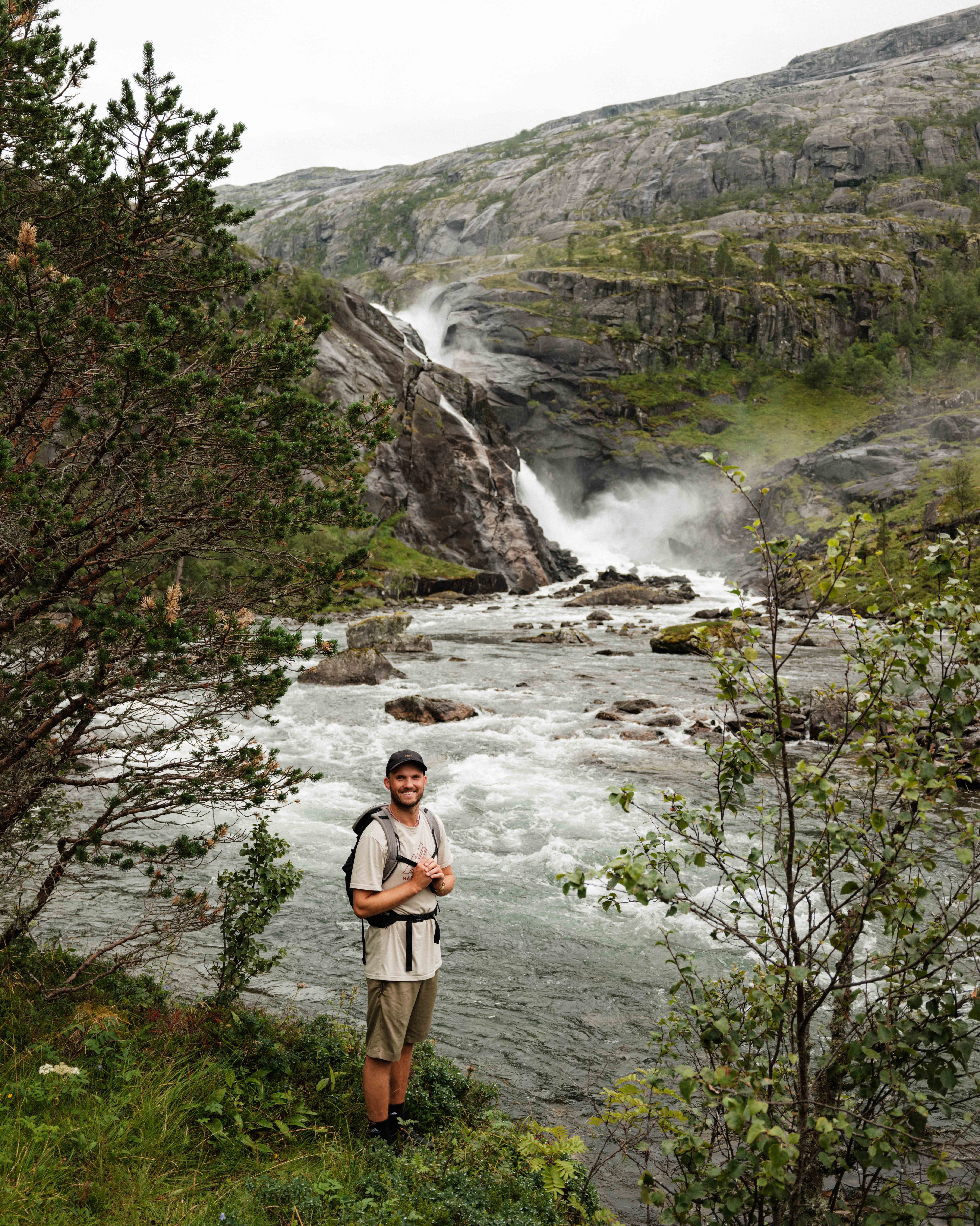 Smiling hiker by the river, with the thundering Nykkjesøyfossen waterfall in the background.