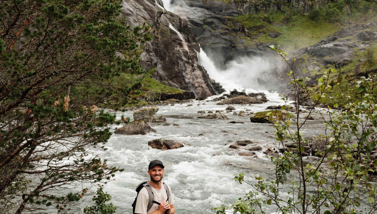 Smiling hiker by the river, with the thundering Nykkjesøyfossen waterfall in the background.