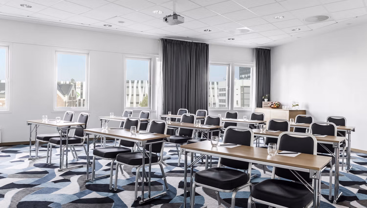 Classroom setup in a meeting room. patterned carpet, two seats per table. Photo