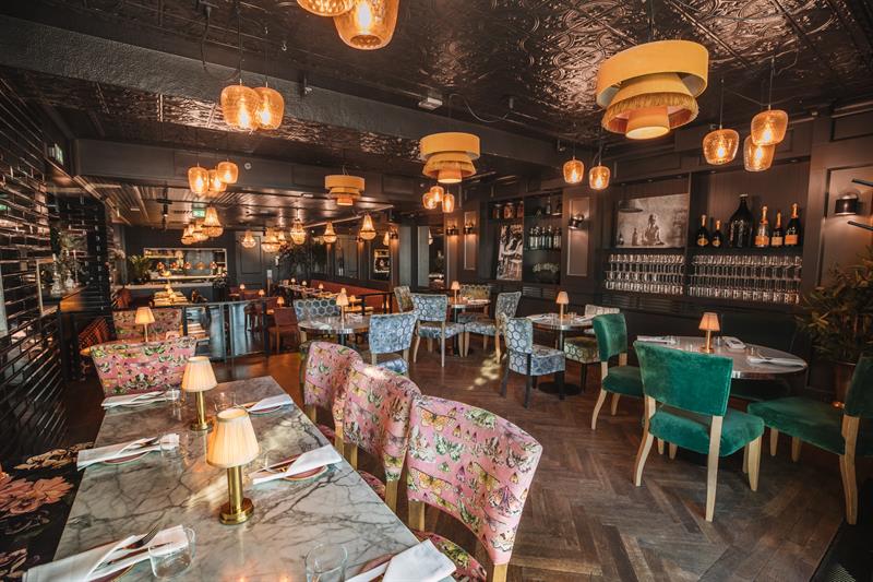 Dark walls, ceiling lamps, various small tables and chairs in different colours.