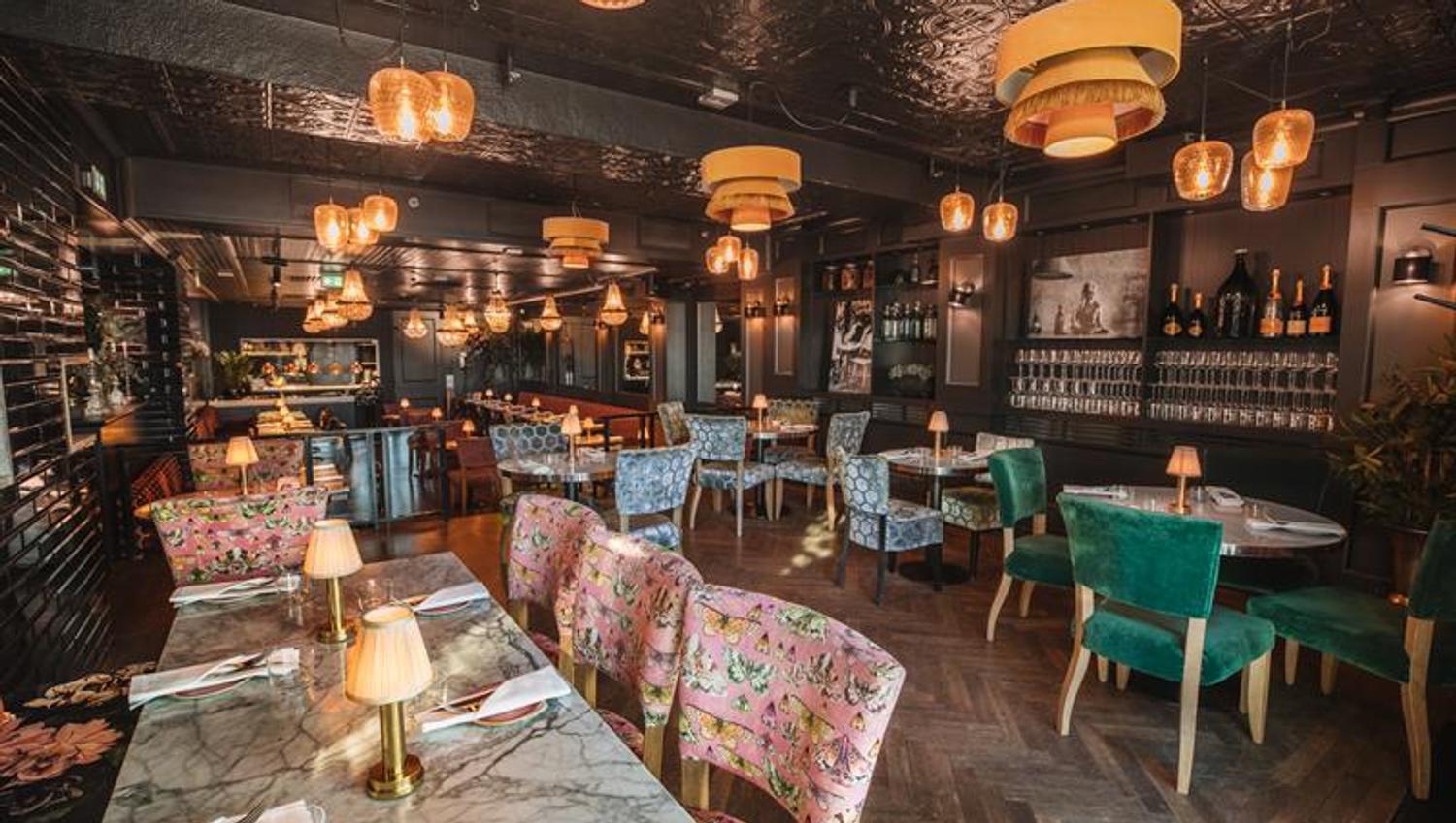 Dark walls, ceiling lamps, various small tables and chairs in different colours.