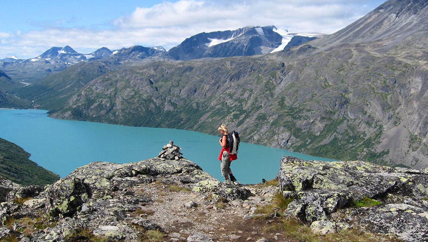 Dame på fjelltur over en fjellrygg over bregrønt vann