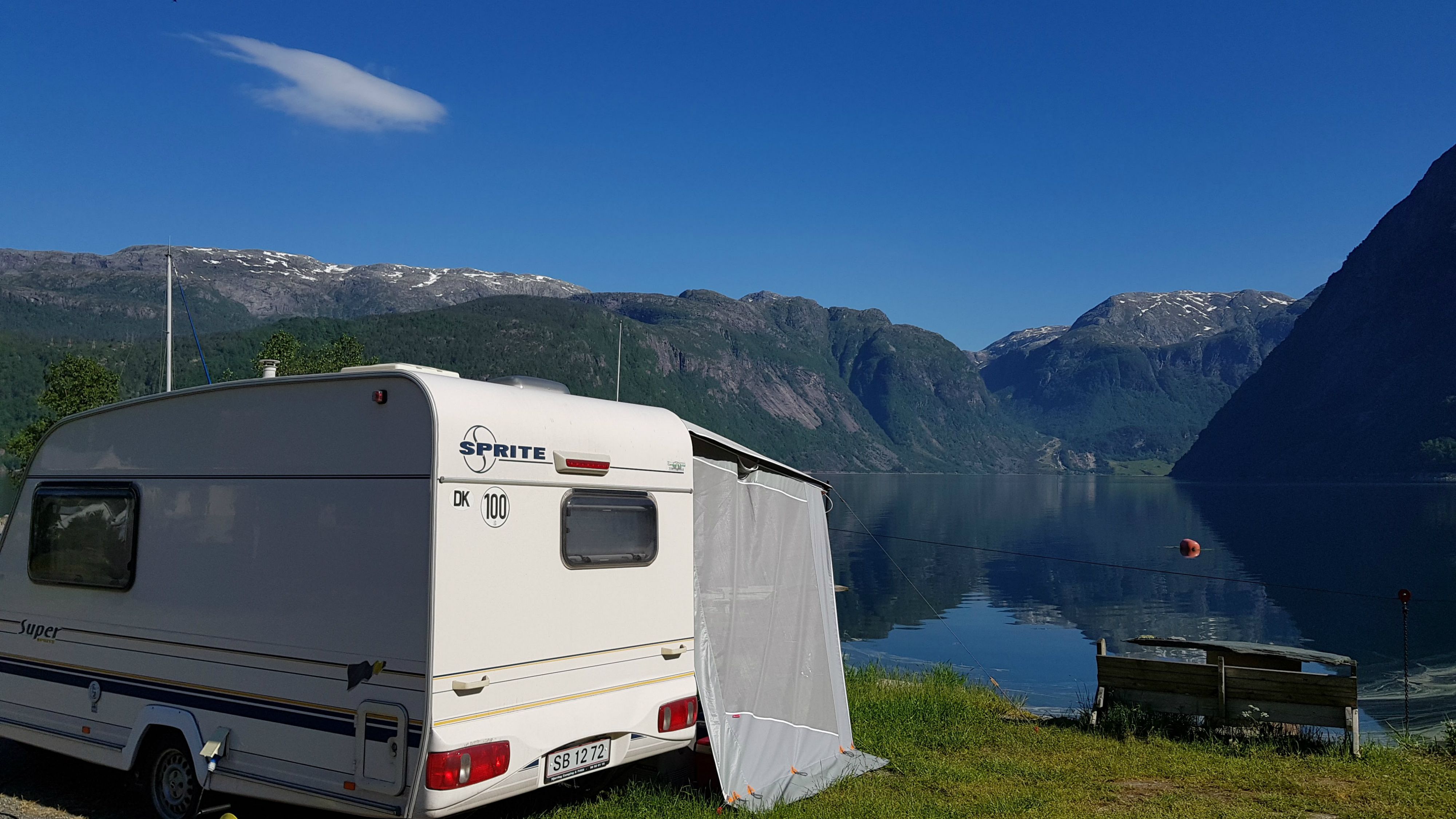 Campingvogn heilt nede ved fjordkanten med utsikt mot fjord og fjell i Hardanger.