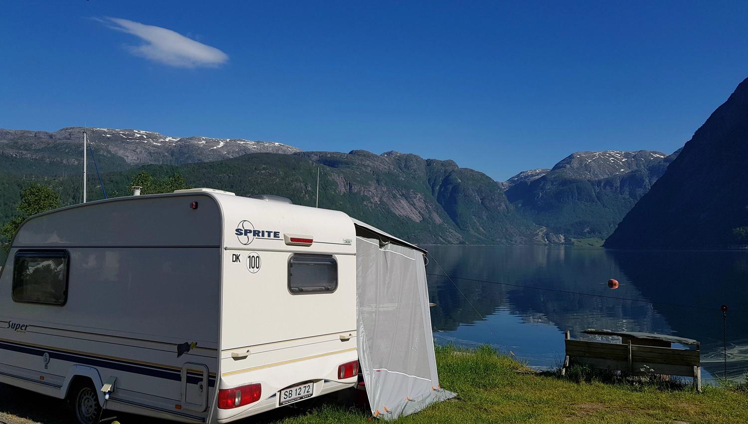 Campingvogn heilt nede ved fjordkanten med utsikt mot fjord og fjell i Hardanger.