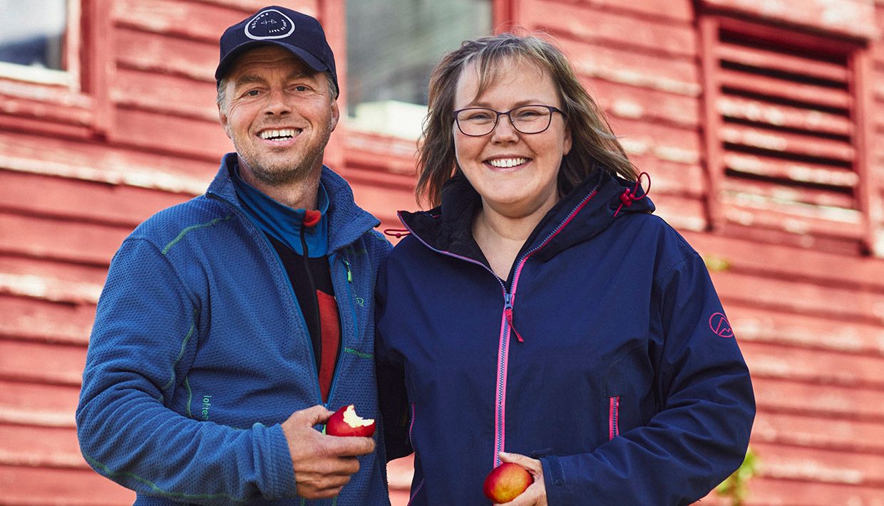 Hosts of Helleland Gard, smiling with fresh apples from the farm.