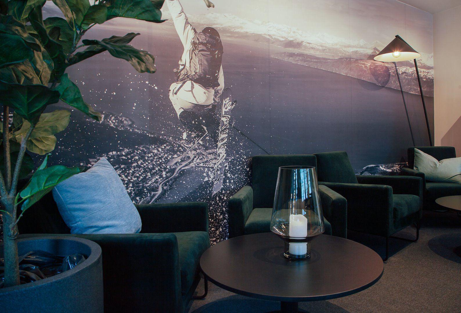Indoor lounge with dark armchairs, round table and candle, floor lamp, and a large ski action mural wall.