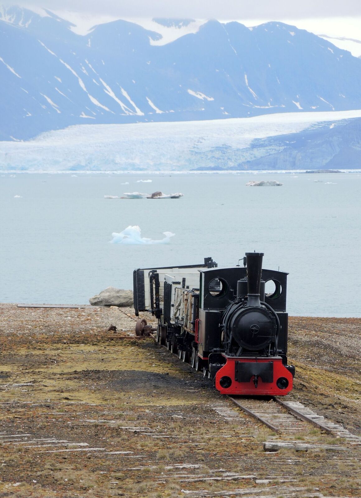 An old locomotive on rails in Ny-Ålesund with a fjord in the background