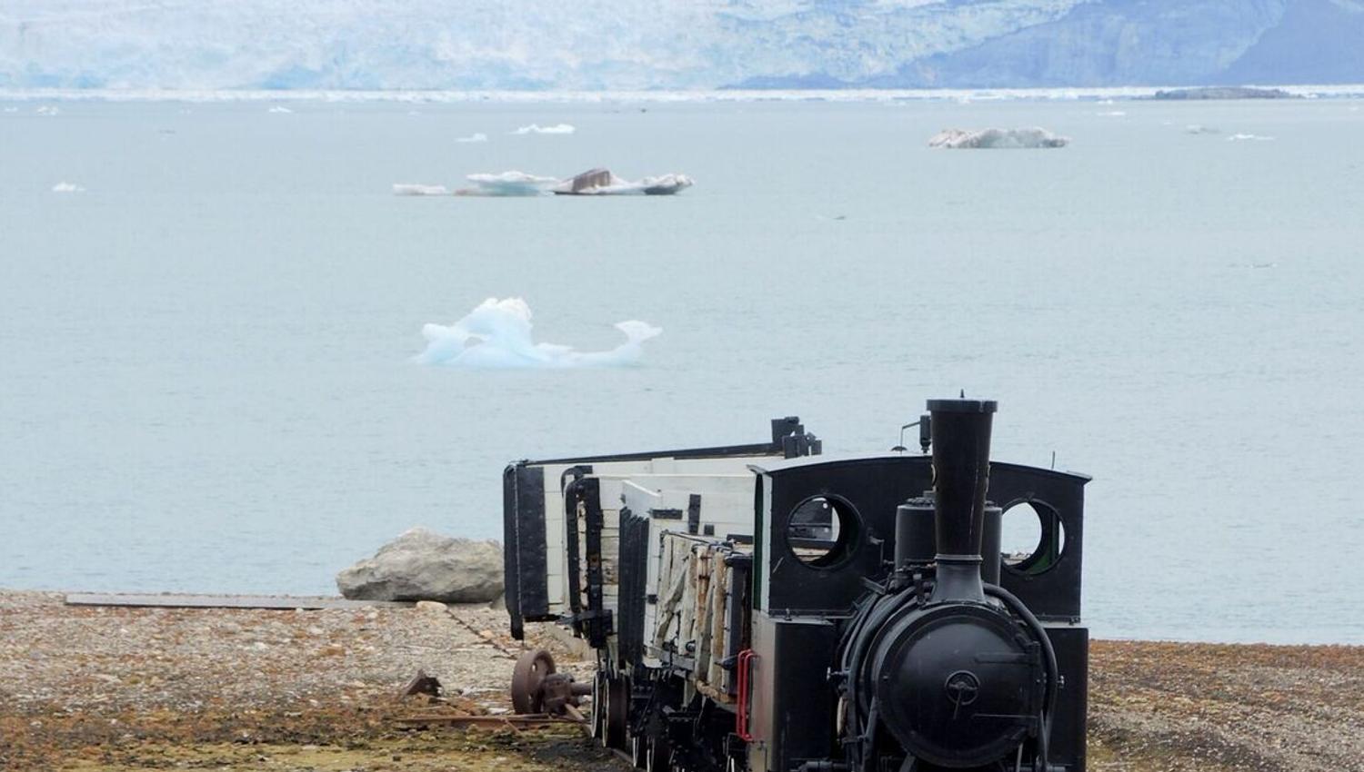 An old locomotive on rails in Ny-Ålesund with a fjord in the background