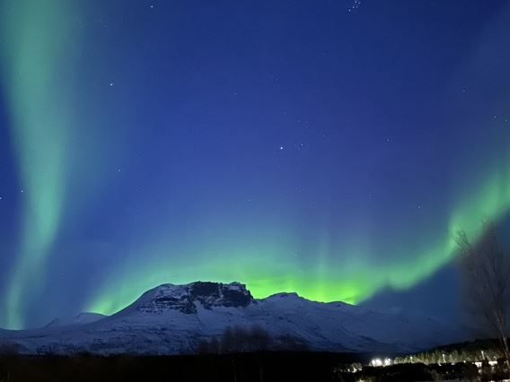 Aurora forms a wavy line behind the mountain
