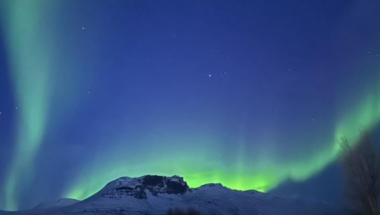 Aurora forms a wavy line behind the mountain