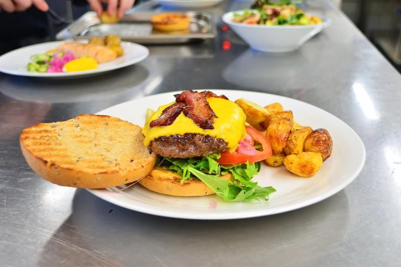 Detaljbilde av cheeseburger med bacon og stekte poteter.