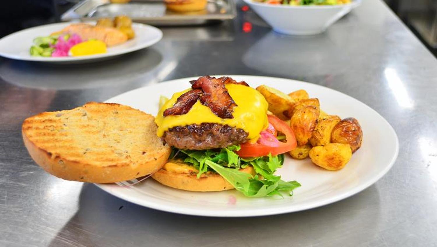 Detaljbilde av cheeseburger med bacon og stekte poteter.