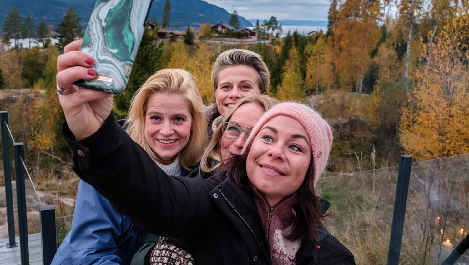 People taking a selfie in a forest area with autumn colors.