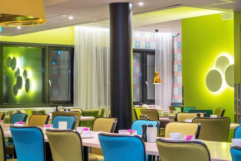 Modern dining area with colourful chairs, green walls, and tables set for a meal.