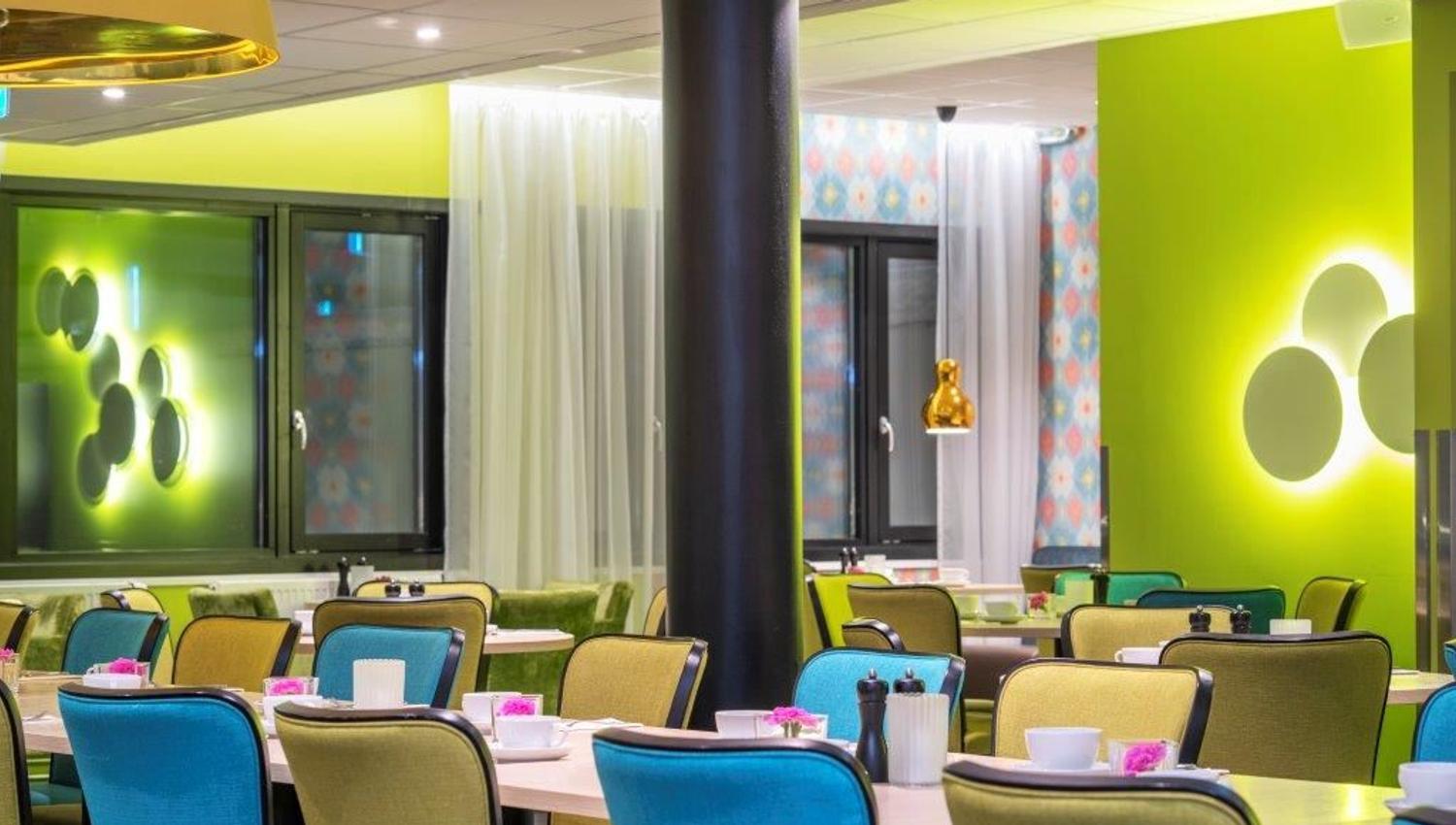 Modern dining area with colourful chairs, green walls, and tables set for a meal.