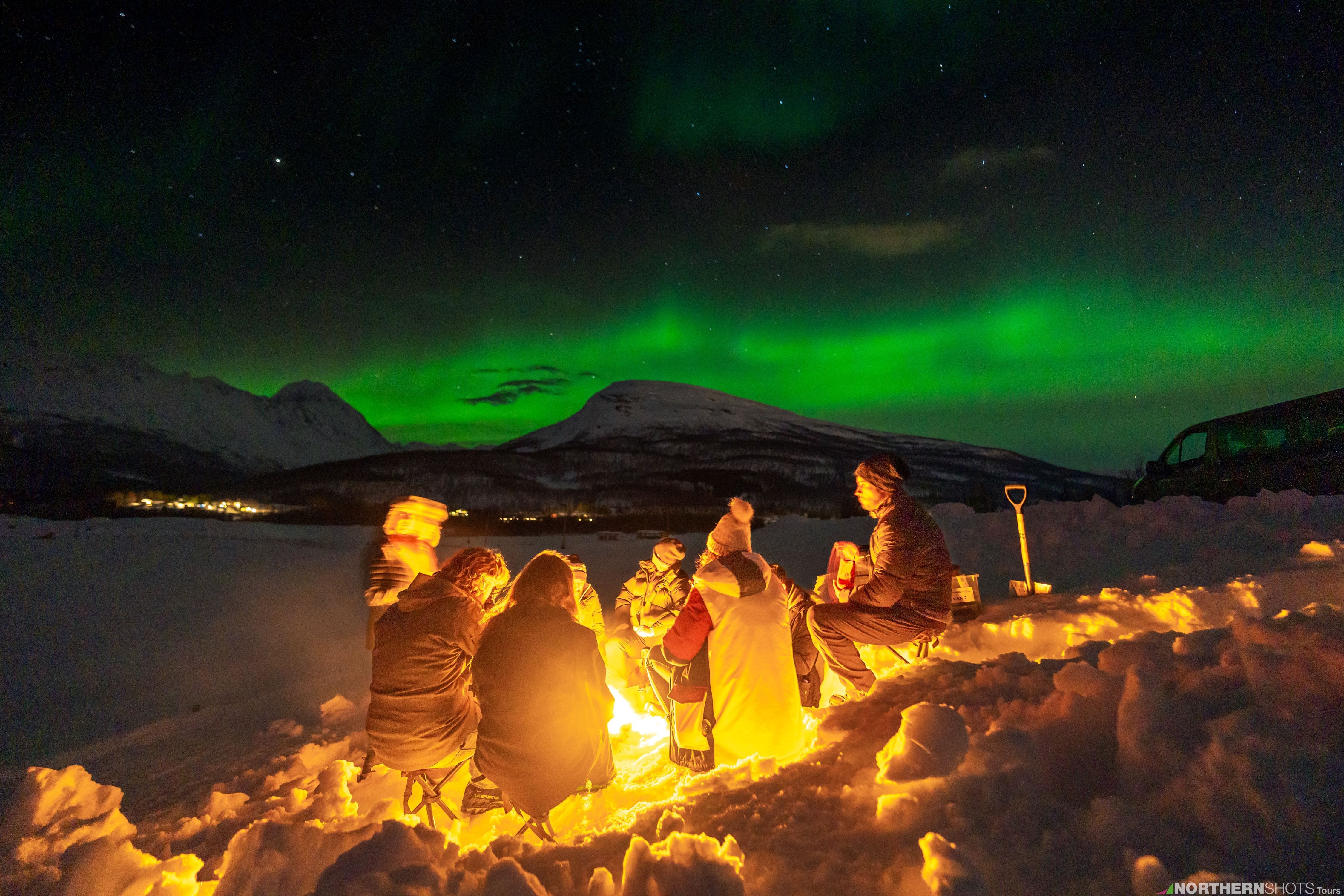 A group of people around a bonfire around under the Northern Lights