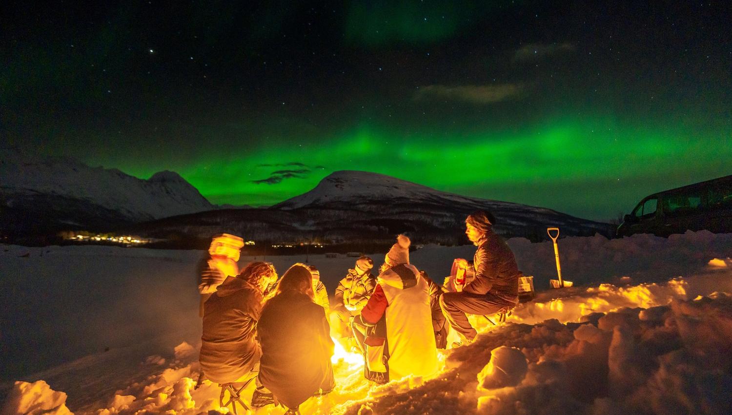 A group of people around a bonfire around under the Northern Lights