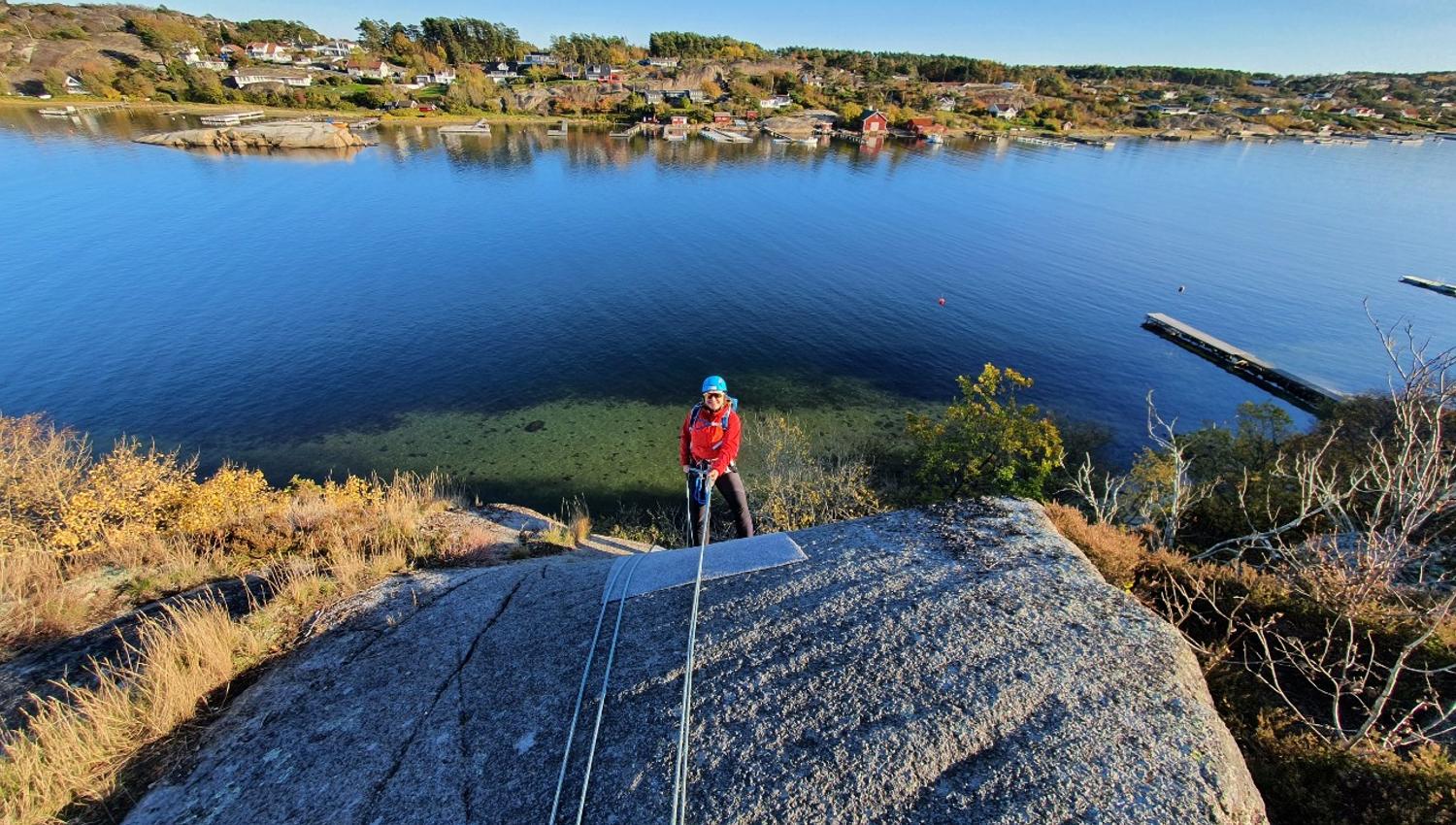 Fantastisk utsikt utover skjærgården mens en jente rappellerer ned fjellet