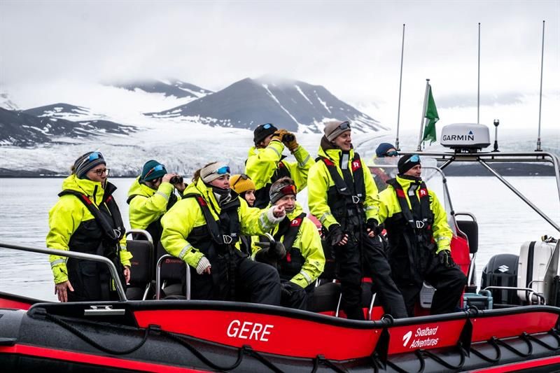 Tourgroup in yellow survival suits on a RIB boat, watching a glacier and mountains.