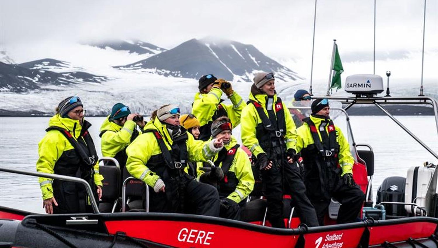 Tourgroup in yellow survival suits on a RIB boat, watching a glacier and mountains.