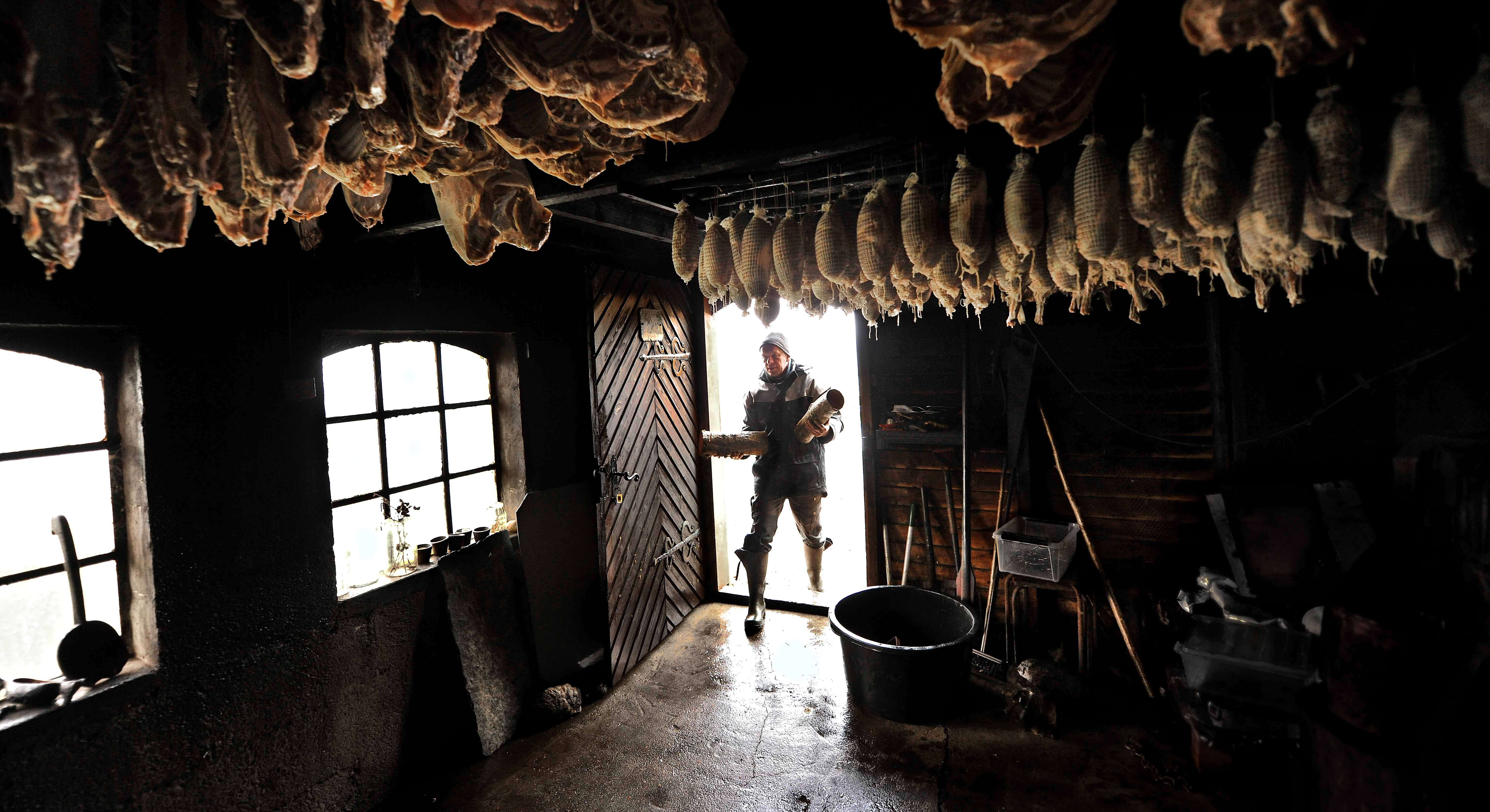 Traditional smokehouse at Syse Gard with hanging cured sausages and a man adding firewood.