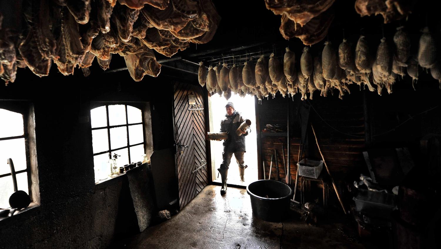 Traditional smokehouse at Syse Gard with hanging cured sausages and a man adding firewood.