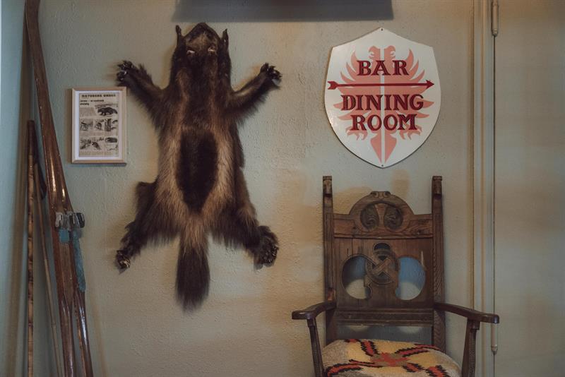 A wall featuring a fox pelt, a sign reading "Bar & Dining Room," and a pair of old wooden skis.