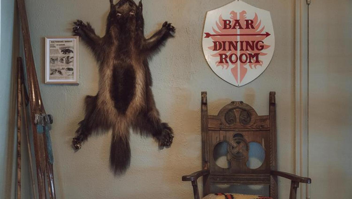 A wall featuring a fox pelt, a sign reading "Bar & Dining Room," and a pair of old wooden skis.