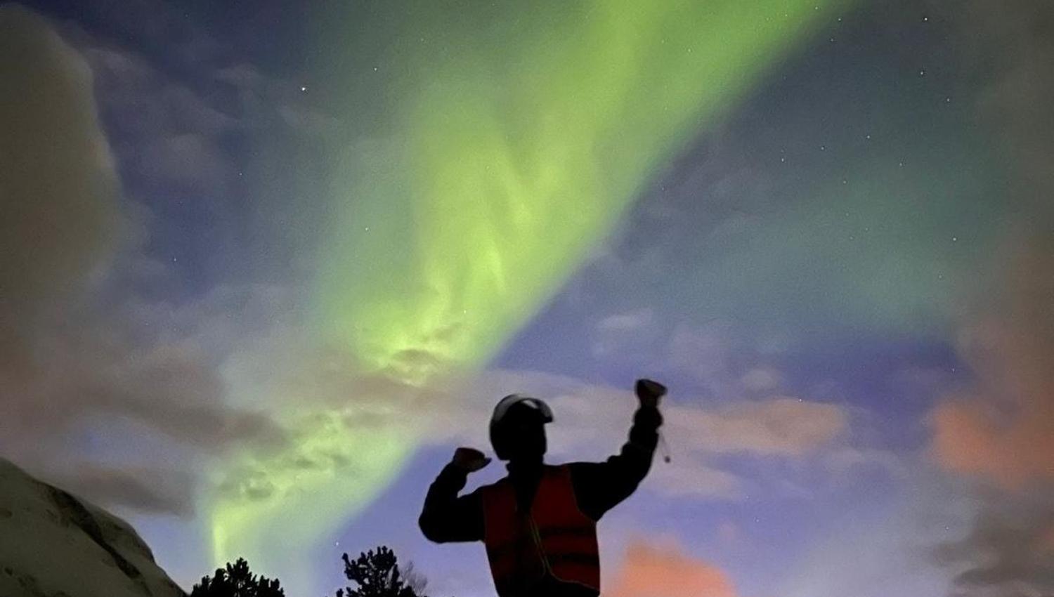 En mann flekser med musklene under nordlyset.