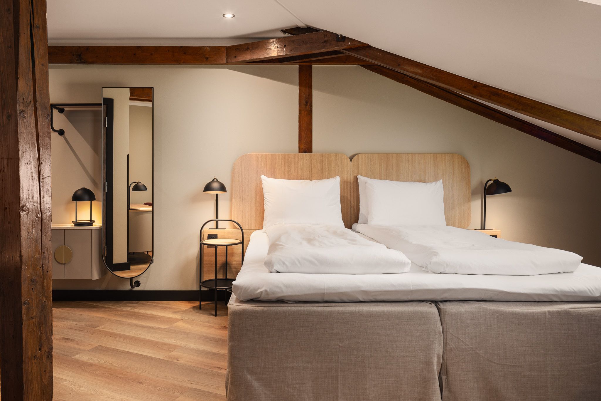 A hotel room interior with a double bed, a mirror, and a brown ceiling beam running along the ceiling.