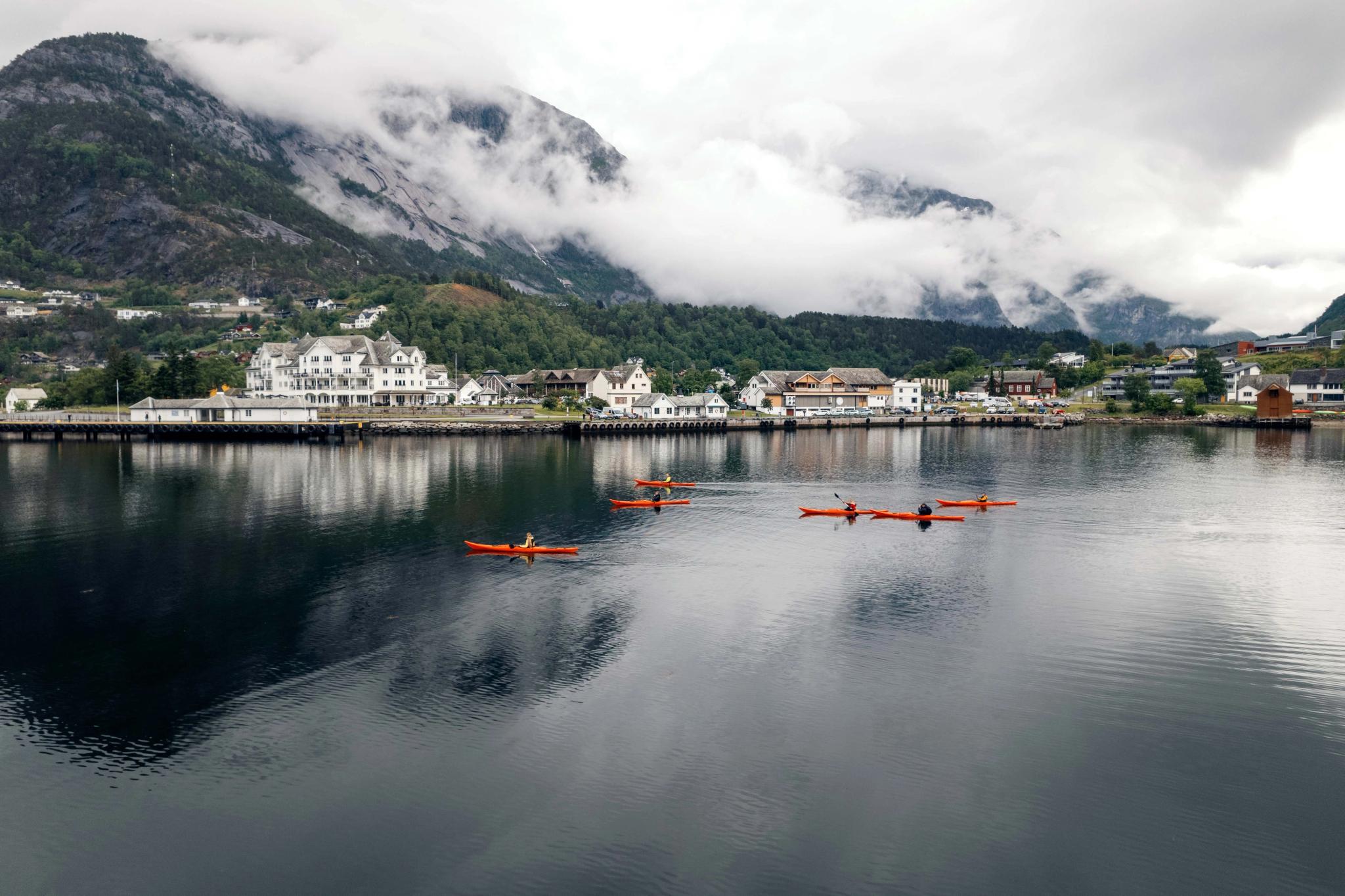 Several red kayaks on the fjord, with the center of Eidfjord in the background.