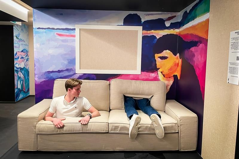 Beige sofa with a boy emerging from a hole, with a pair of legs appearing through a different hole next to him.